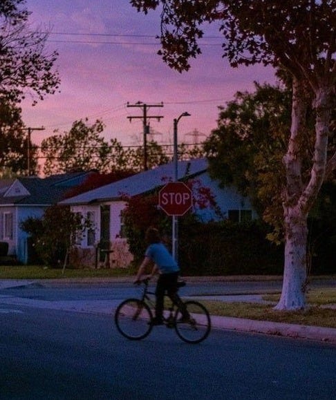 This may contain: a person riding a bike down the street at dusk with a stop sign in front of them