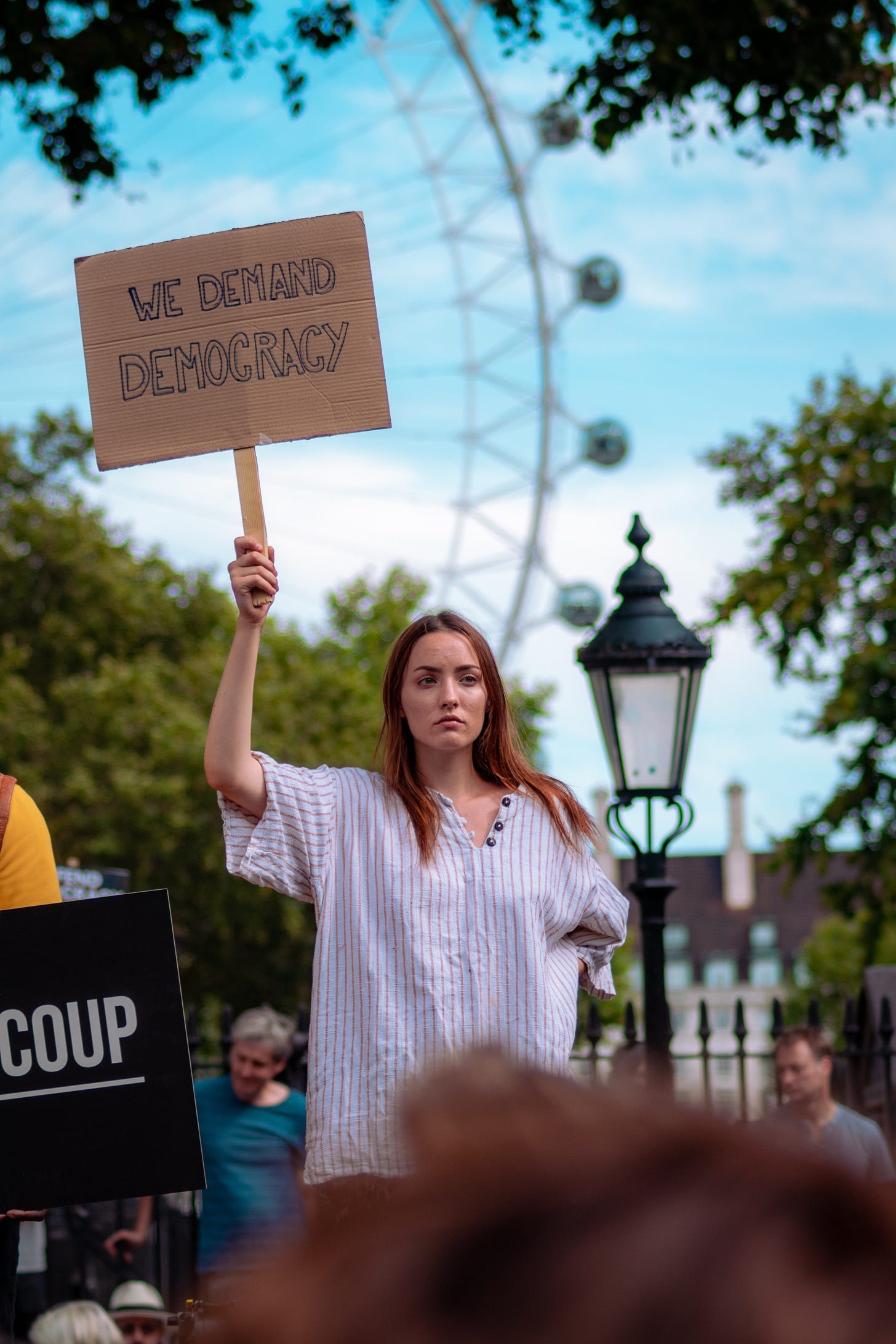 A photo of a young woman at a rally in London with a sign demanding democracy