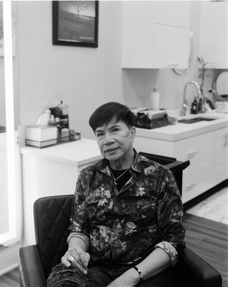 Black and white half body portrait photo of Glenn Rivera sitting in his salon