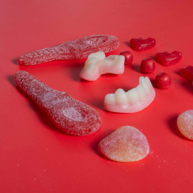 An assortment of red gummies and candies, including two pieces of teeth-shaped gummies in the middle and two marshmallow on the right -- FDA coverage from STAT