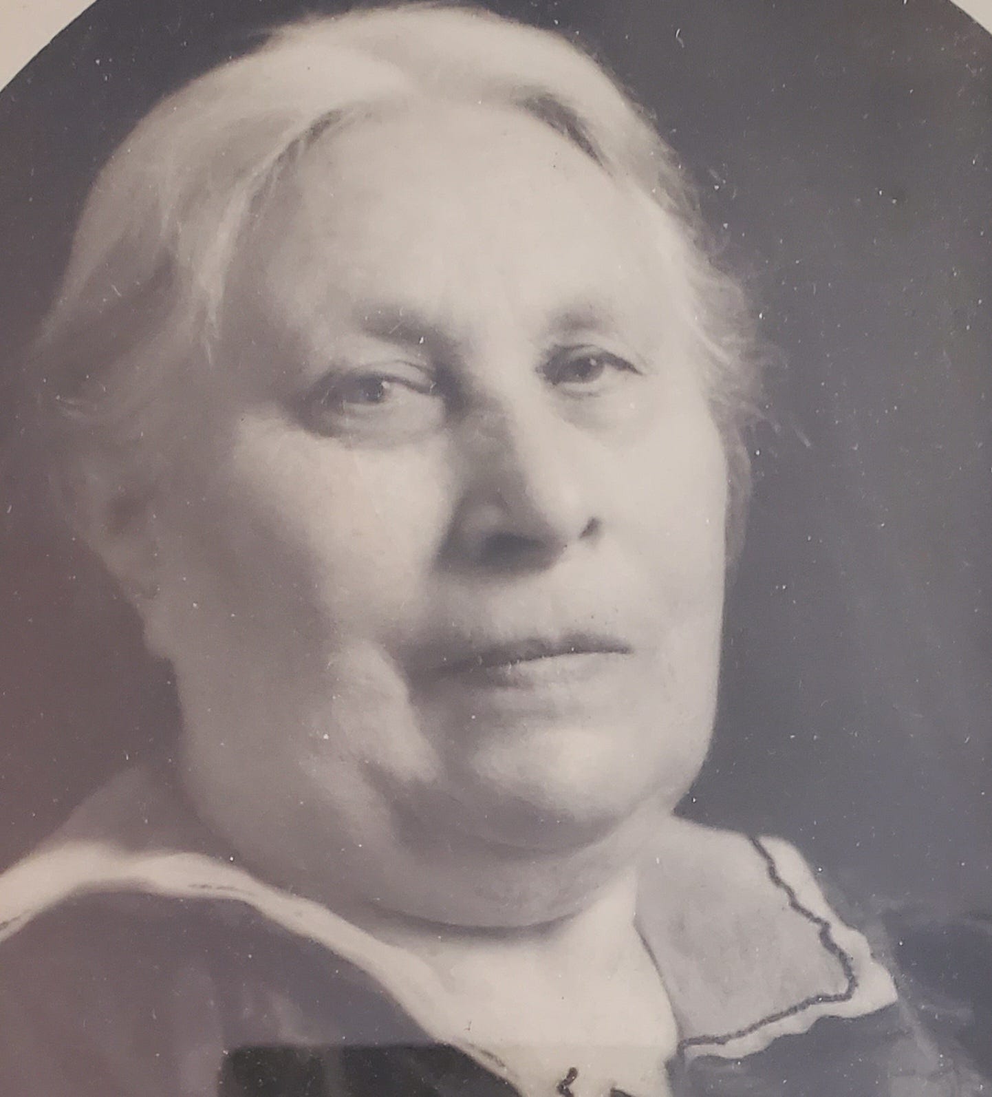 A black and white photo portrait of an older white woman with gray hair pulled back and a round face