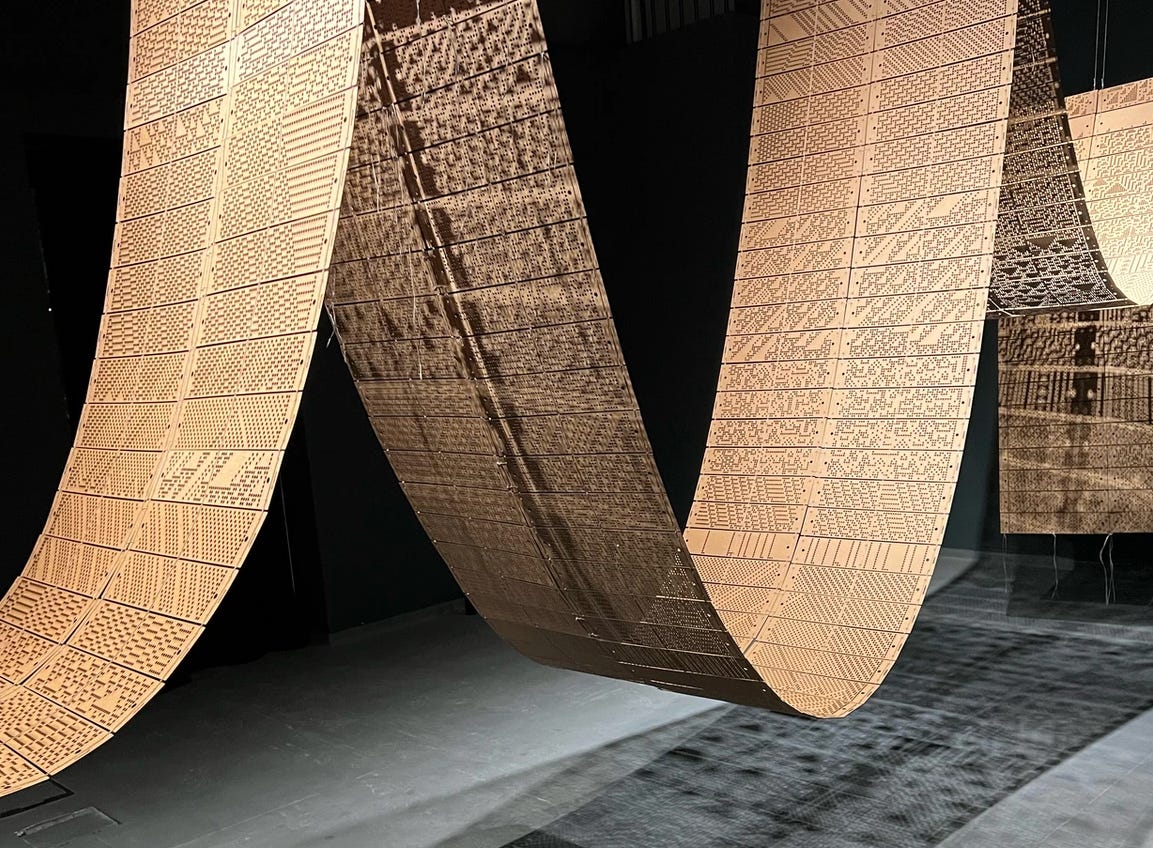 Photo shows N/A-A, an artwork made up of perforated punch cards, an early method of codifying computer instructions, stitched together and suspended from the continuous chain in a gallery space by the artist Merve Mepa.