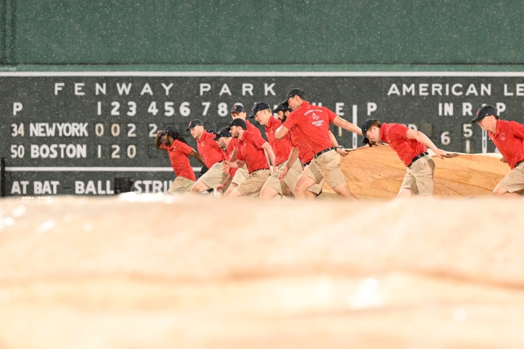 Members of the grounds crew cover the infield with a tarp during a rain delay in the fourth inning of a game between the New York Mets and the Boston Red Sox at Fenway Park on July 21, 2023