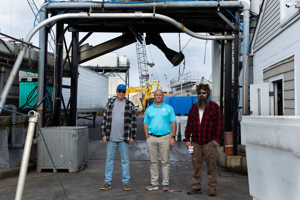 William Bright, Wayne Reichle and Stefan Axelsson, dressed in casual clothing, standing by what appears to be a warehouse on a fishing dock. 