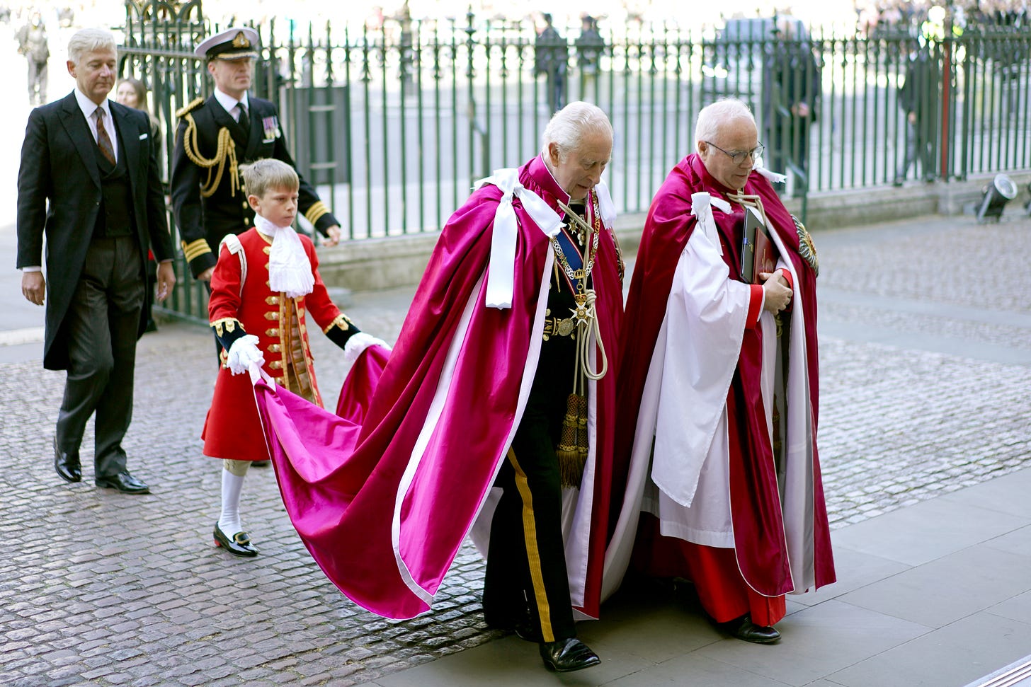 King Charles in a pink gown with a boy holding the train