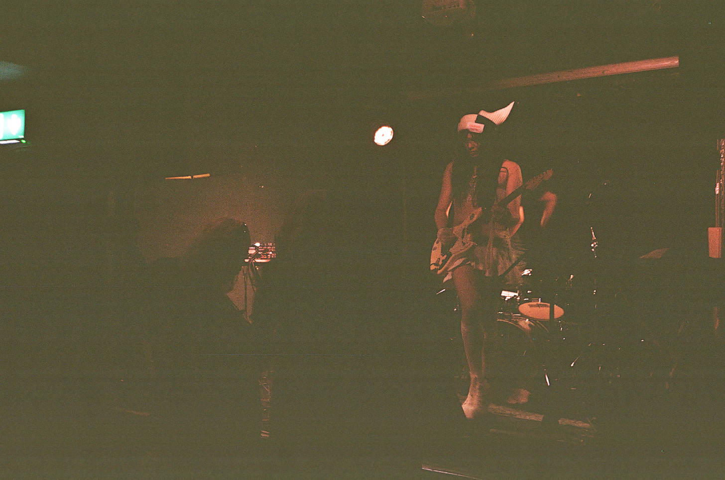 In a 35mm film photo, red light illuminates an otherwise black scene, in which Princess Xixi plays electric guitar onstage