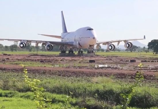 A somewhat run down 747 sits in an empty, muddy field during daylight hours