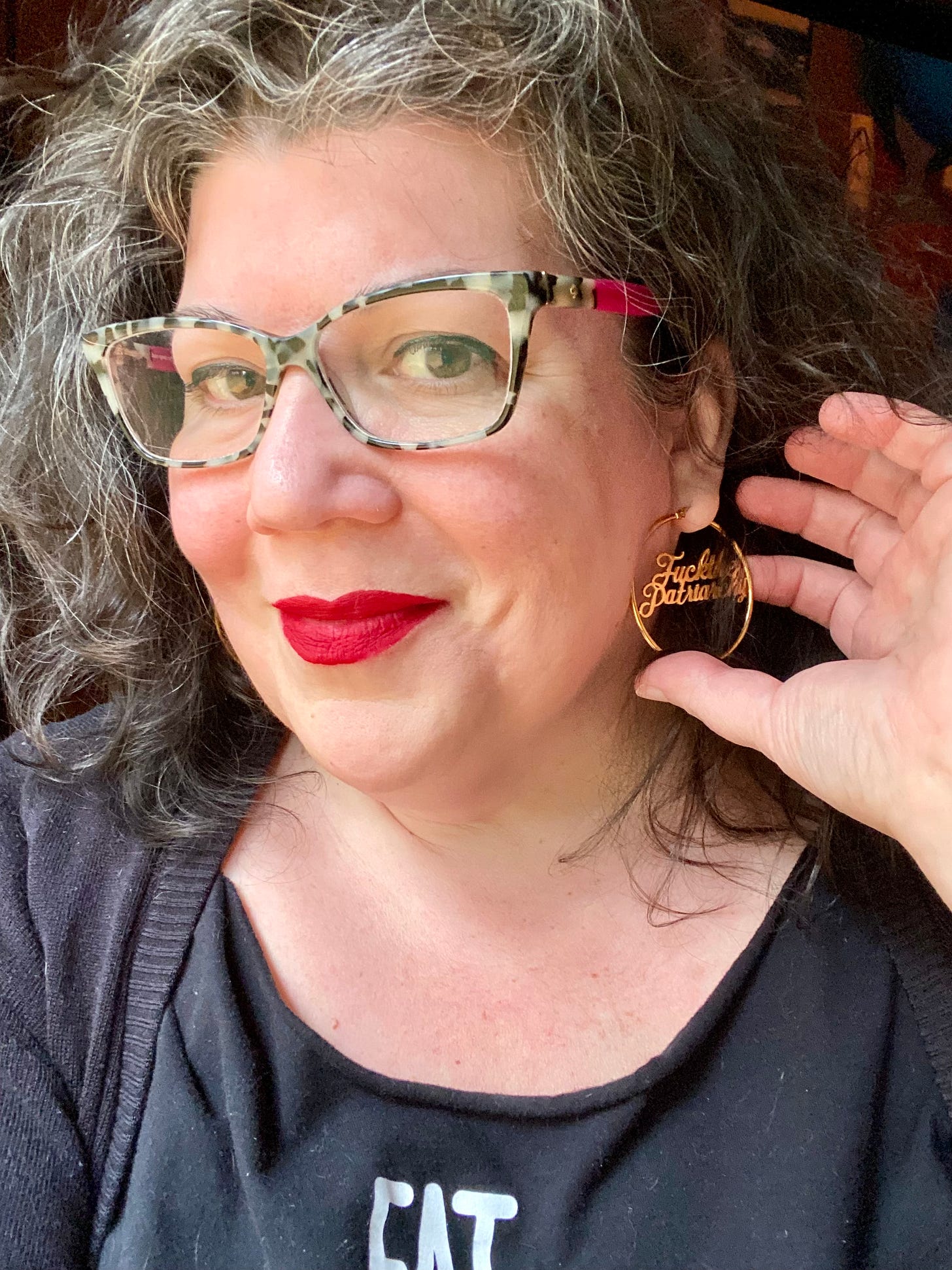 Headshot of Hanne Blank Boyd, a white middle-aged woman with grey and brown curly/frizzy hair, bright red lipstick, and grey tortoiseshell rimmed eyeglasses.