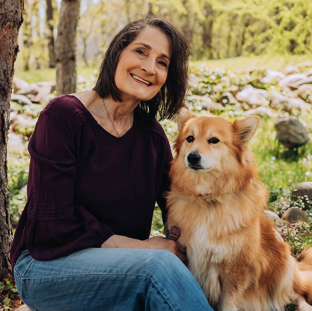 Woman and rust colored dog sit near a tree in the grass