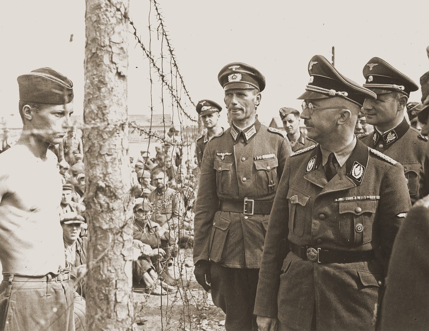Heinrich Himmler looks at a young Soviet prisoner during an official visit to a POW camp in the vicinity of Minsk.  

His Chief of Staff, Karl Wolff, can be seen by Himmler's left shoulder.