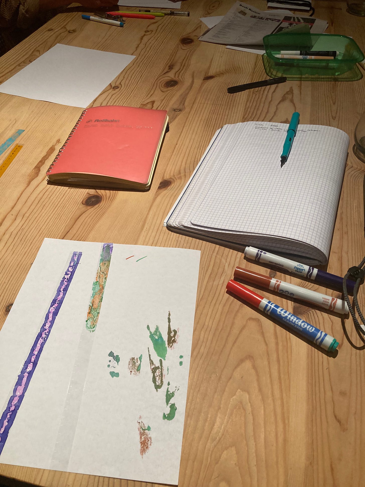 Strips of film stock colored with marker, notebooks, and markers on a wooden table