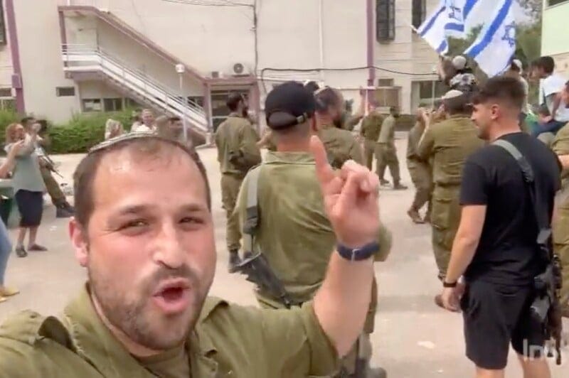 A man in an Israeli army uniform gestures at an Israeli flag