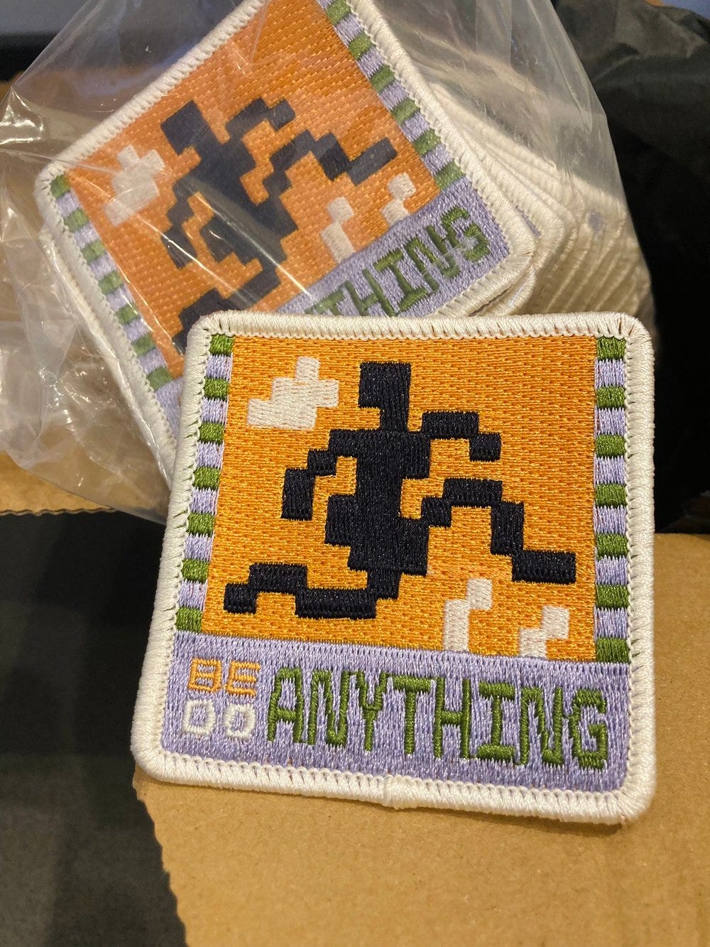 Photo of an embroidered patch that has the words "BE/DO ANYTHING"