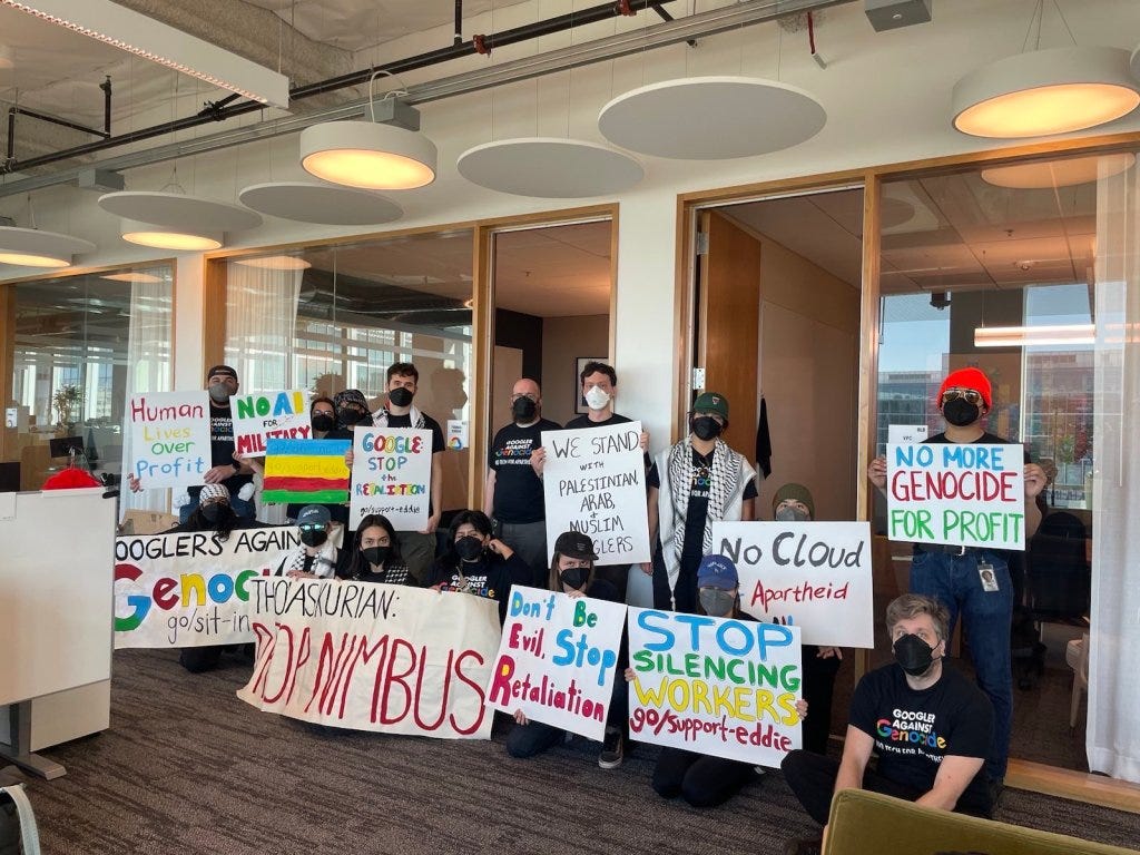 A large group of Google employees hold signs protesting their company's participation in "Project Nimbus."