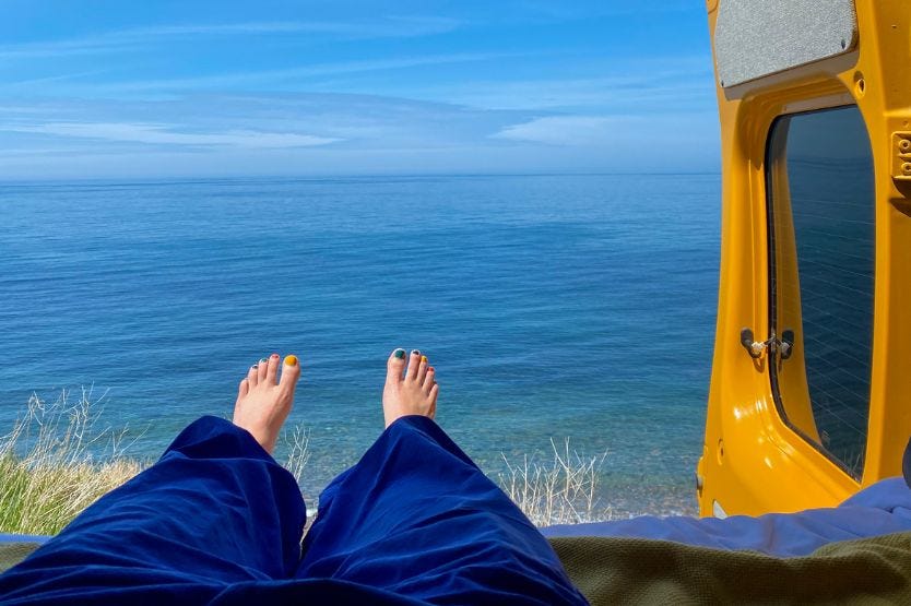 An ocean view out the back bed doors of our converted campervan, with my feet hanging off the edge of the mattress