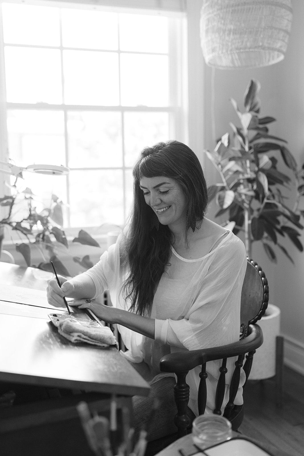 A black and white photo of me sitting at my drafting table, painting and smiling 