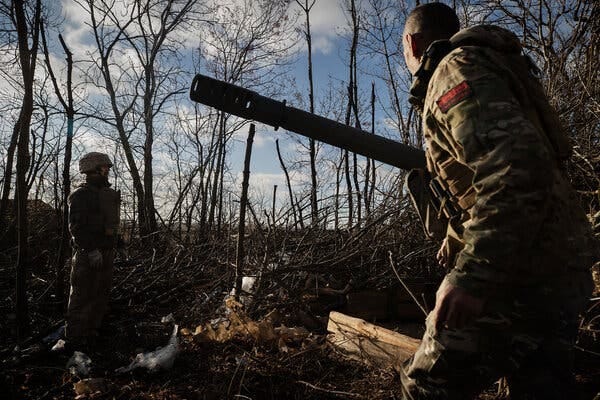 Soldiers with military equipment in a forested area.