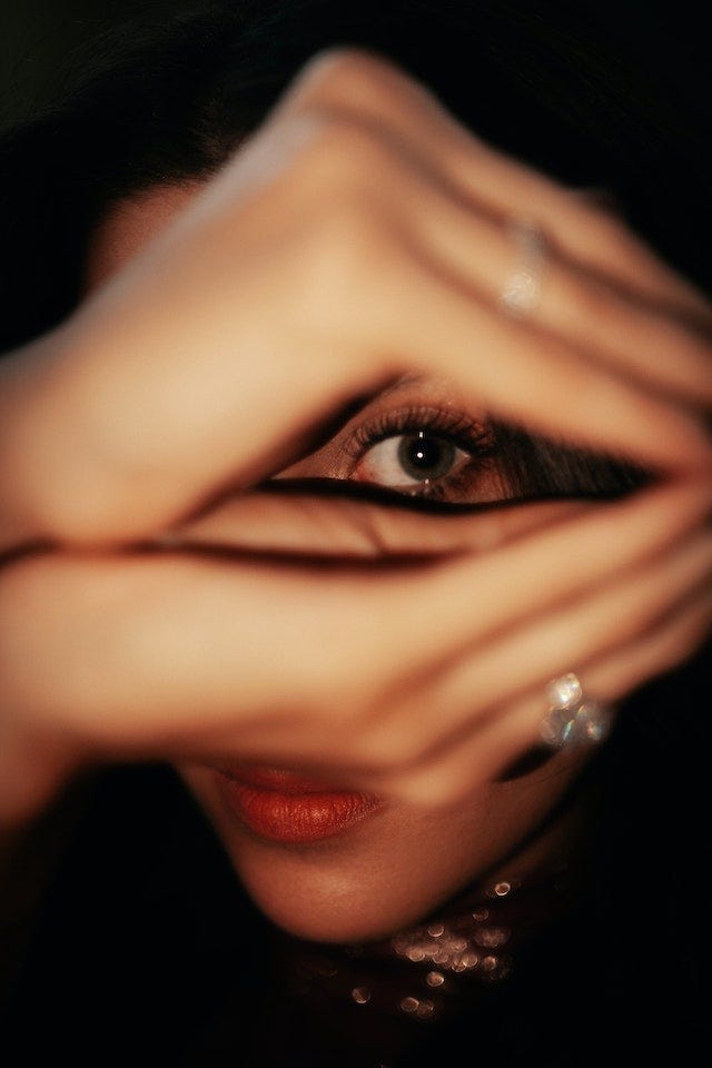 A woman holding her hands in a diamond shape, with her eye peering through the gap between her hands.