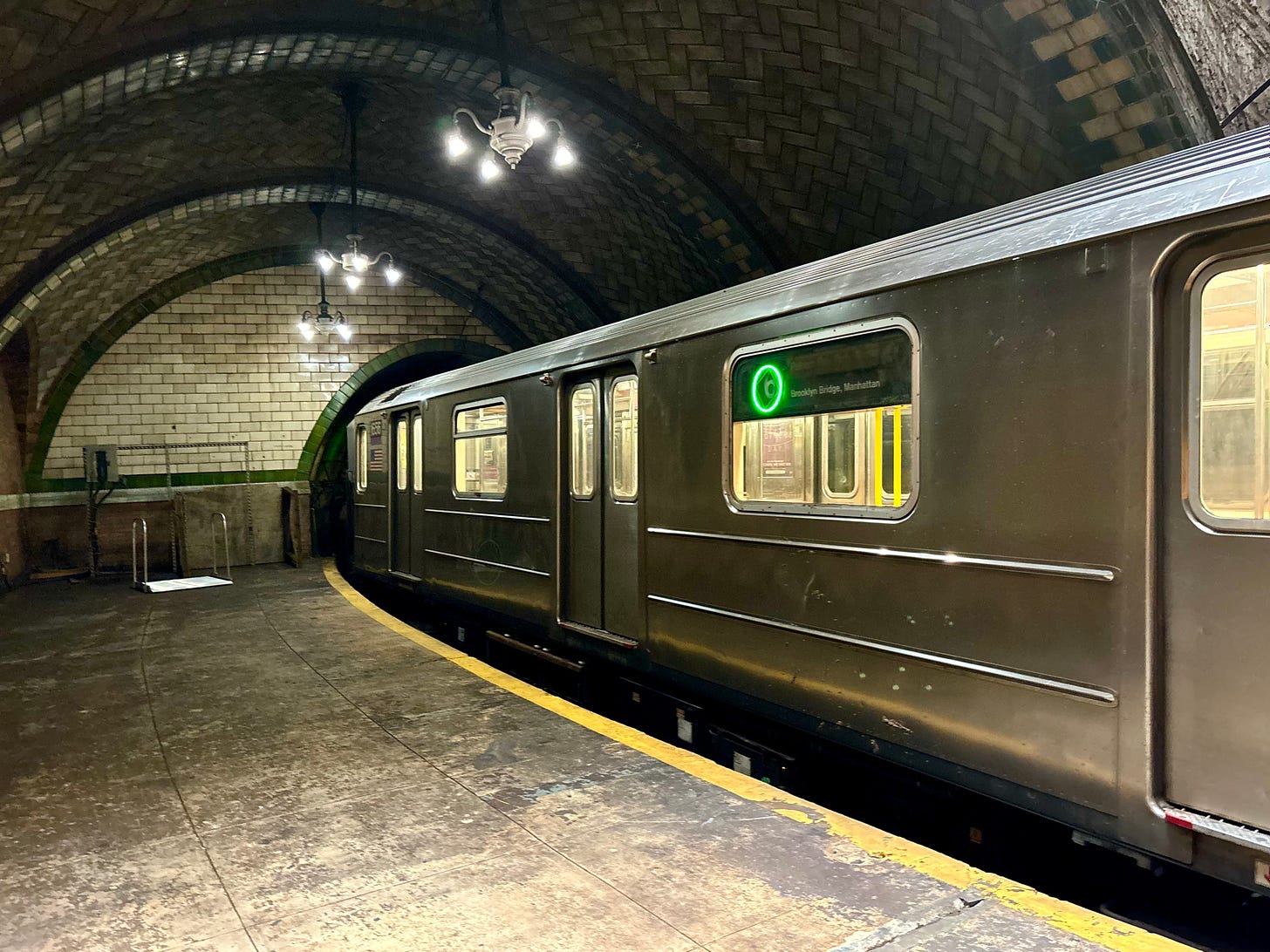 A 6 Train pulled into the station. The curve of the platform means there is a foot to two-foot gap between the platform and the doors. To the side there is what looks like the handles from a diving board on a white piece of plastic.