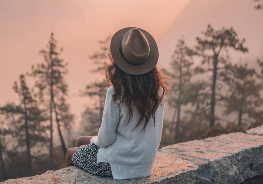 Contemplative woman sitting on rocky mountain outcrop during rose sunset