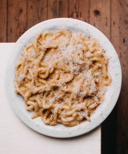 A plate of cacio e pepe pasta on a white plate, on top of a white table next to a wooden floor