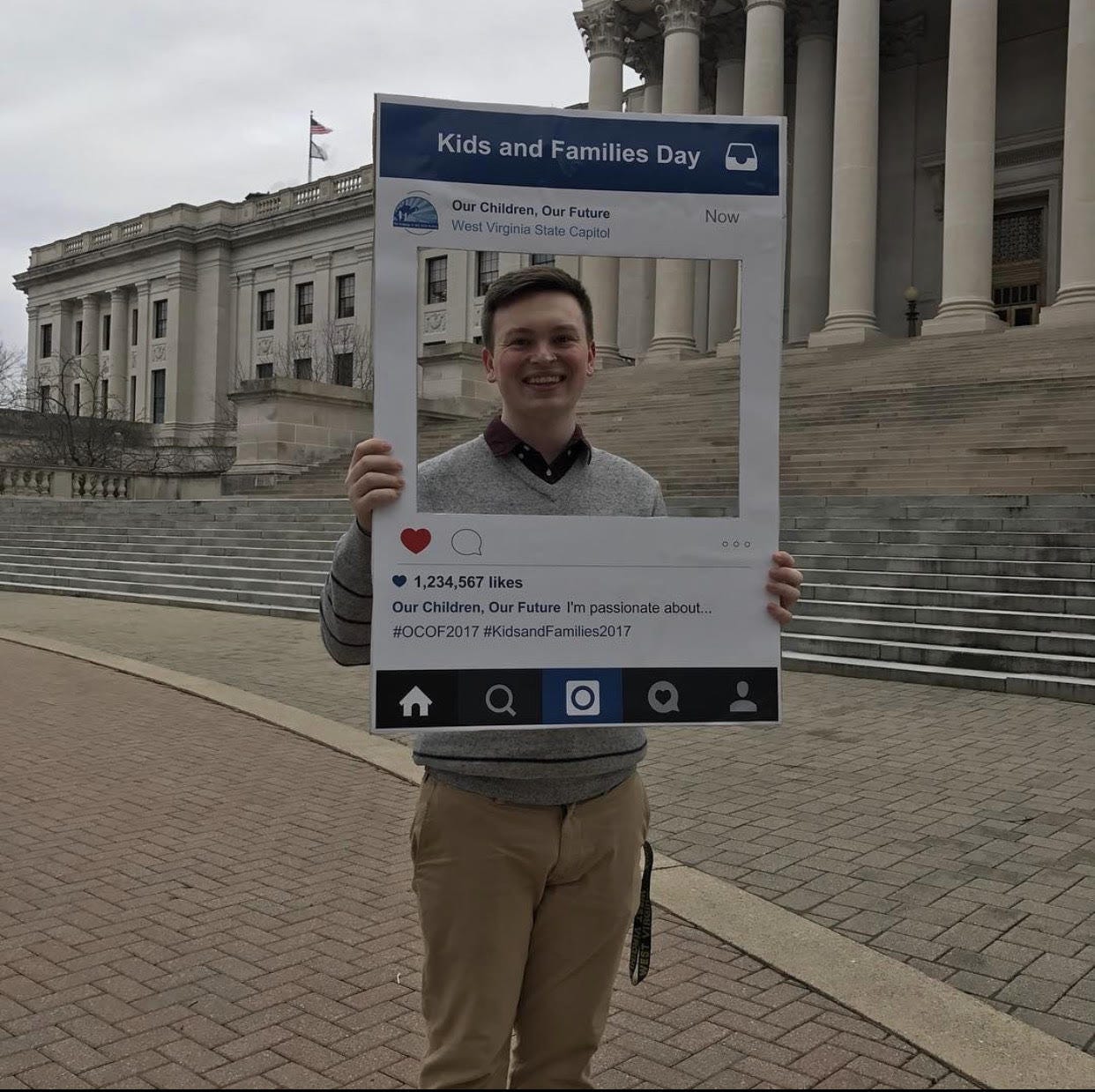 Justice holds a cardboard cut-out that looks like an instagram post in front of the steps of the West Virginia Capitol Building
