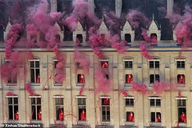 Red smoke and ribbons billow across Paris' rooftops during a performance involving multiple headless Marie Antoinettes