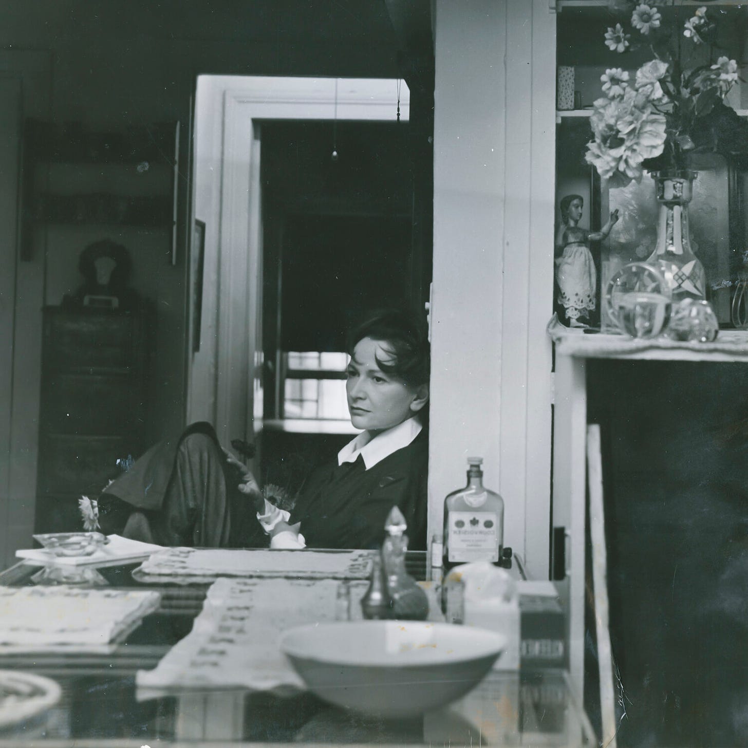 Foto de la artista Hedda Sterne sentada en la mesa de su estudio mirando con aire pensativo