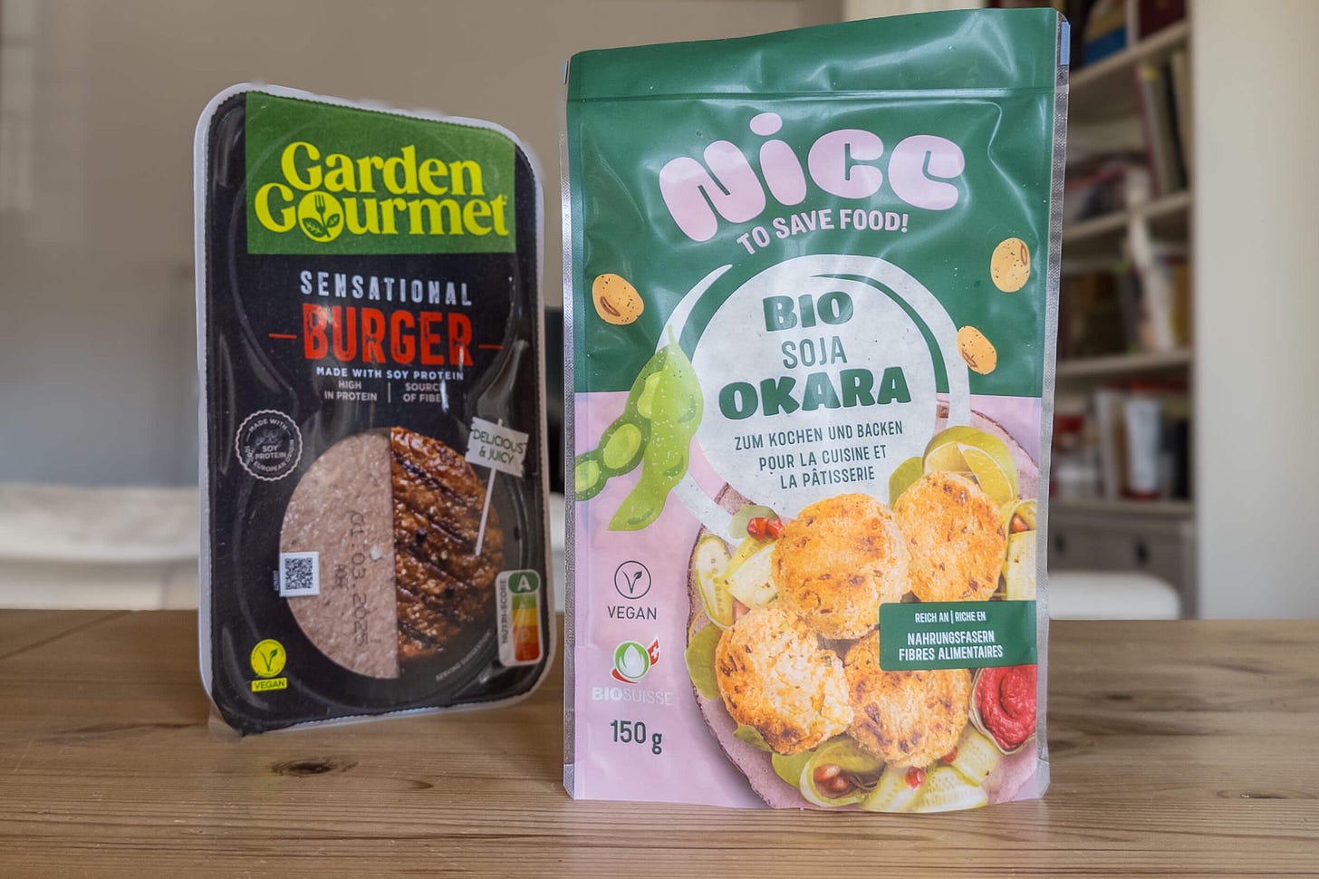 Auf einem Holztisch stehen zwei Produkte nebeneinander: links eine Packung vegande ‚Burger‘ aus Soja, rechts ein grüner Beutel ‚Nice to Save Food Bio Soja Okara‘ von Coop, hergestellt aus Sojaresten bei der Tofu-Produktion. Auf einem Holztisch stehen zwei Produkte nebeneinander: links eine Packung vegande ‚Burger‘ aus Soja, rechts ein grüner Beutel ‚Nice to Save Food Bio Soja Okara‘ von Coop, hergestellt aus Sojaresten bei der Tofu-Produktion.