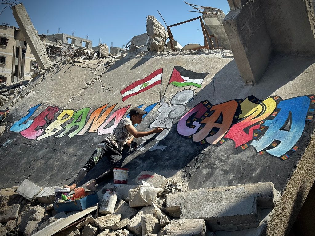 Displaced Palestinian artist Jamil al-Baz, 22, paints a mural on the rubble of destroyed homes in Khan Younis expressing solidarity with Lebanon, September 26, 2024. (Photo: Doaa Albaz/APA Images)