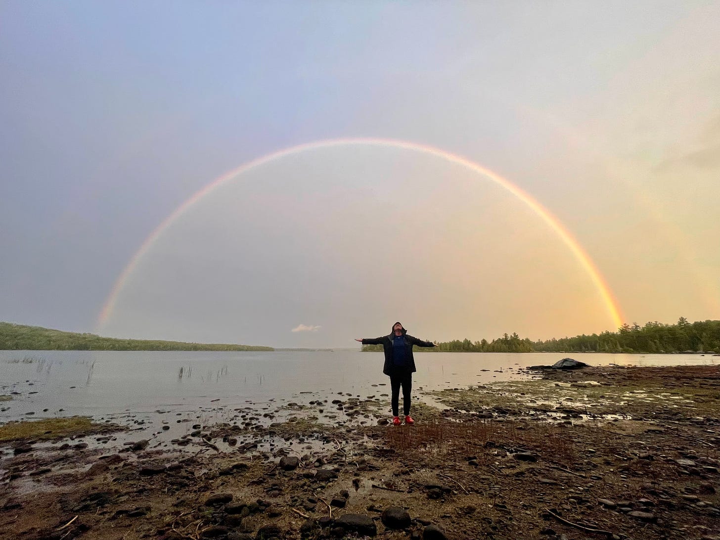 Woman under rainbow, arms outstretched.