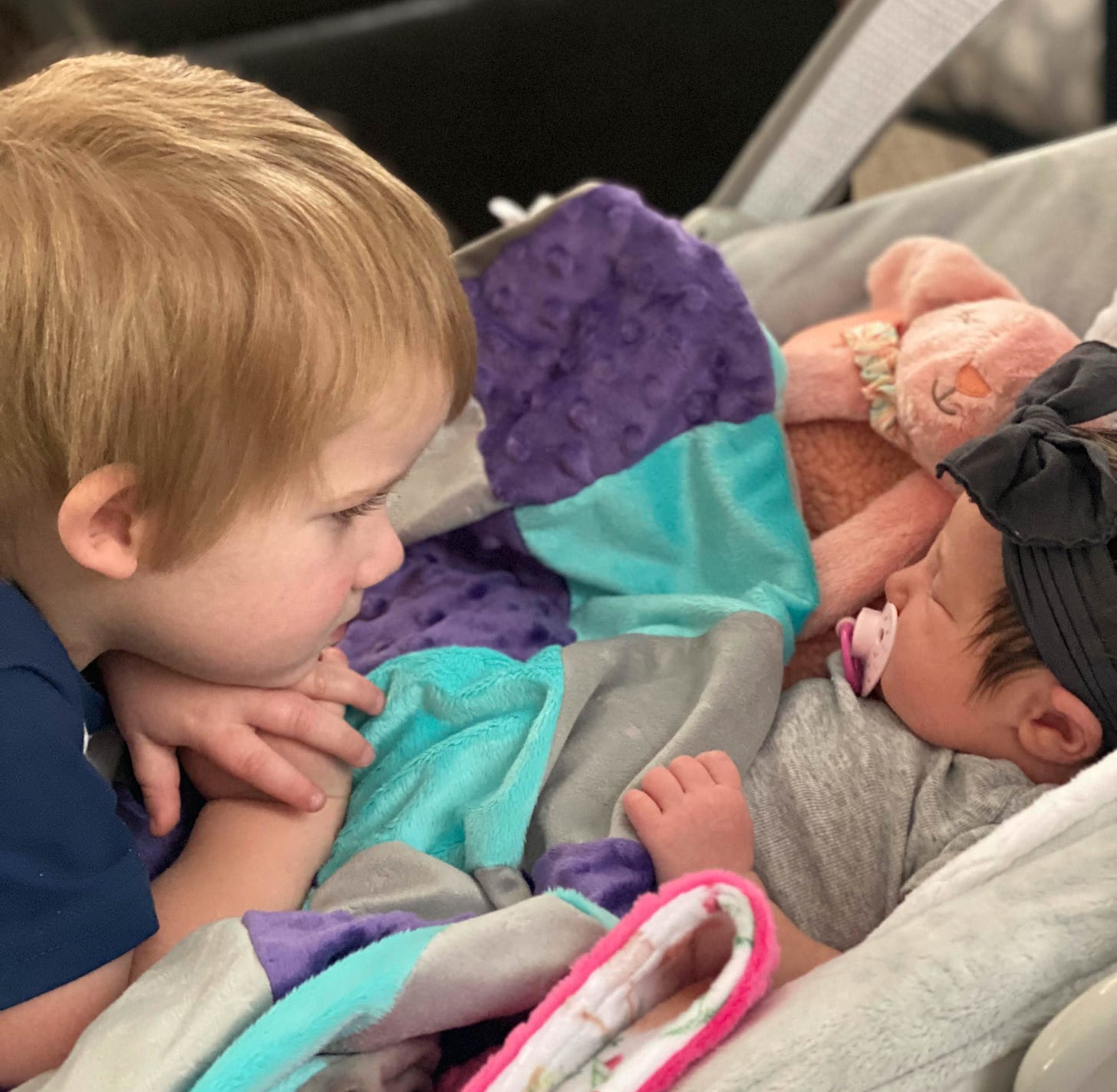 Toddler boy looking intently at baby sister sleeping in bouncy seat.