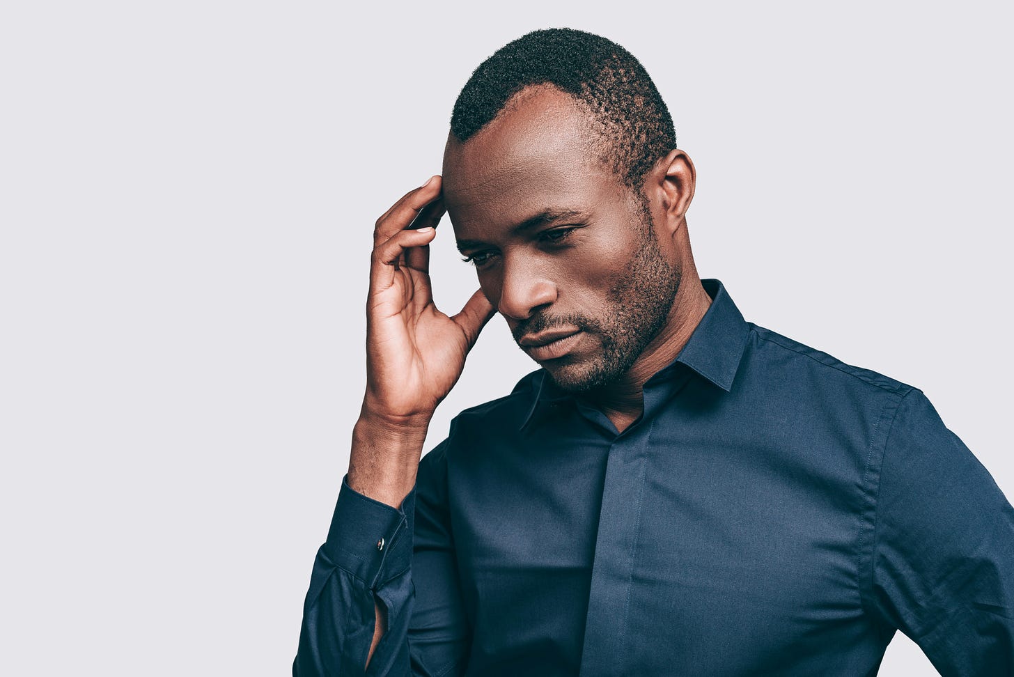 Black man standing in front of white wall with hand on forehead looking worried