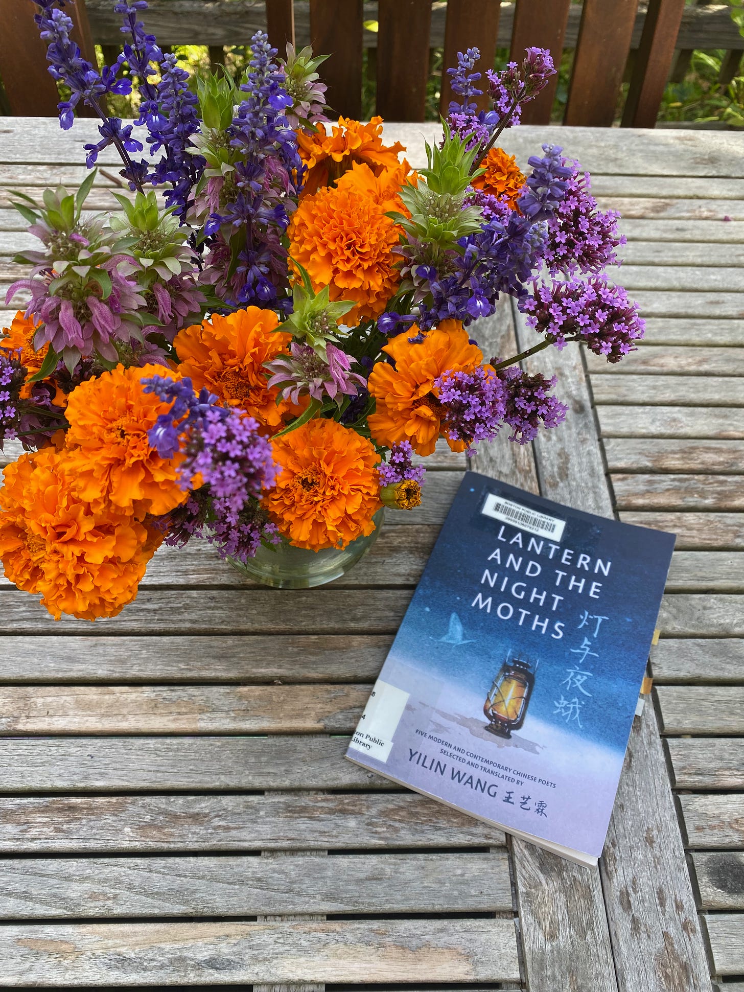 The Lantern and the Night Moths on a placemat next to a vase of purple and orange flowers.