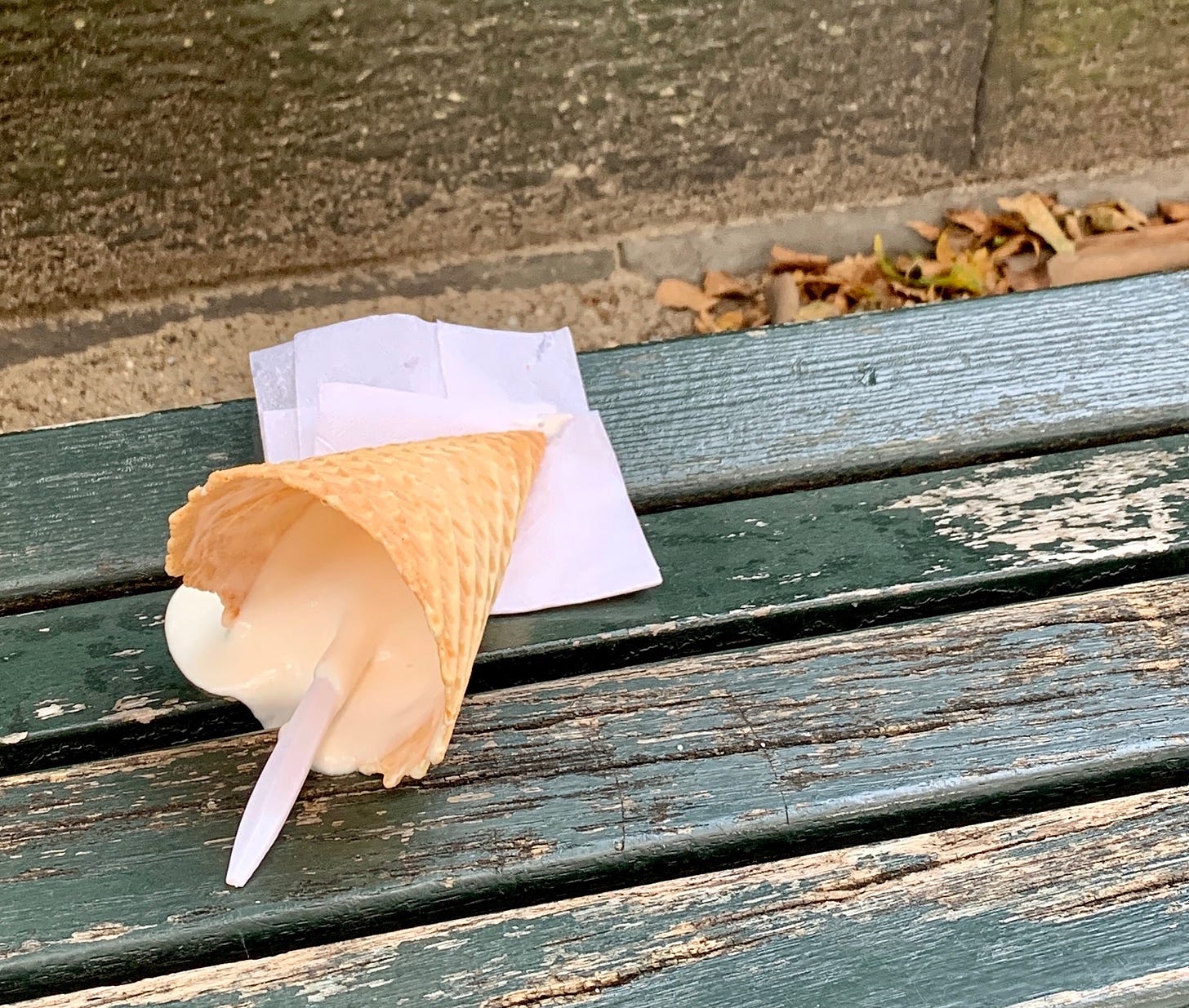 an abandoned waffle cone slowly melting out on a park bench