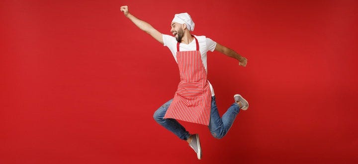 Funny young male chef cook or baker man in striped apron white t-shirt toque chefs hat posing isolated on red background. Cooking food concept. Mock up copy space. Jumping, fooling around, having fun.