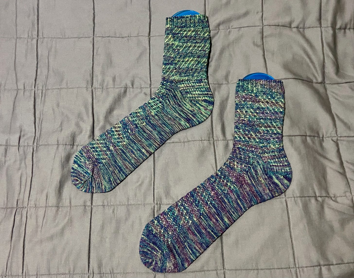A completed pair of Dear Björn socks in variegated green/blue/purple yarn. They're placed on top of sock blockers.