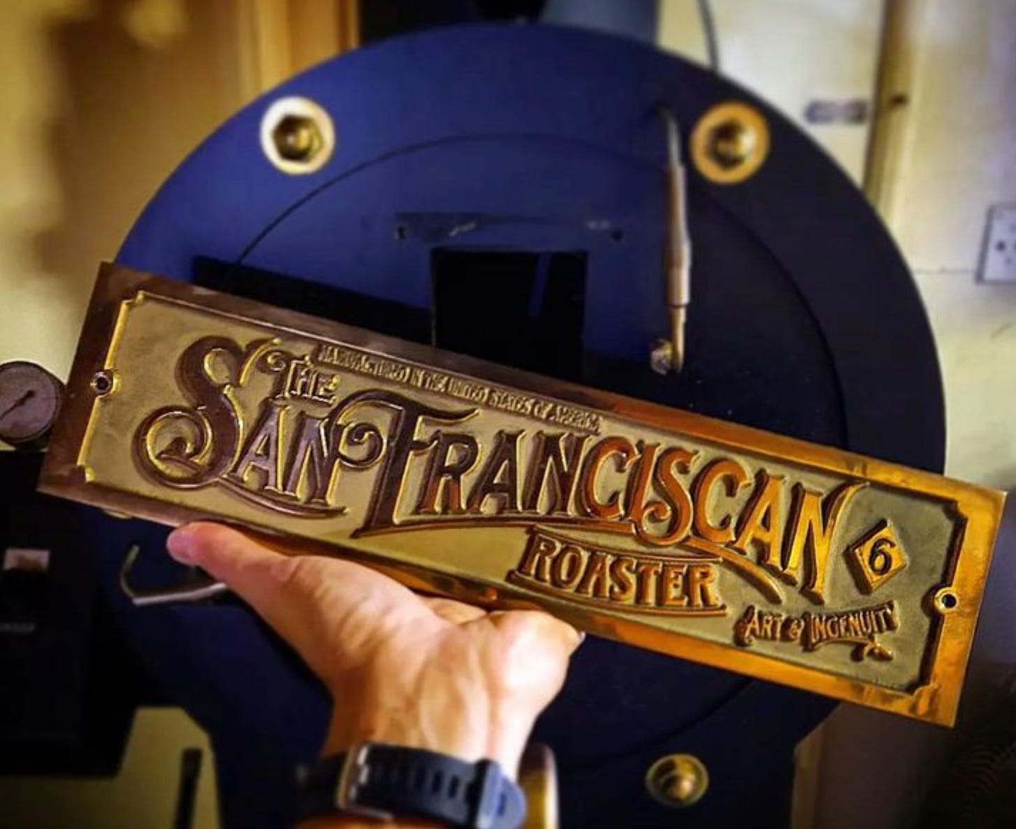A close up of the gold plaque found on San Franciscan Coffee Roasters that says the name and motto, "Art in ingenuity."