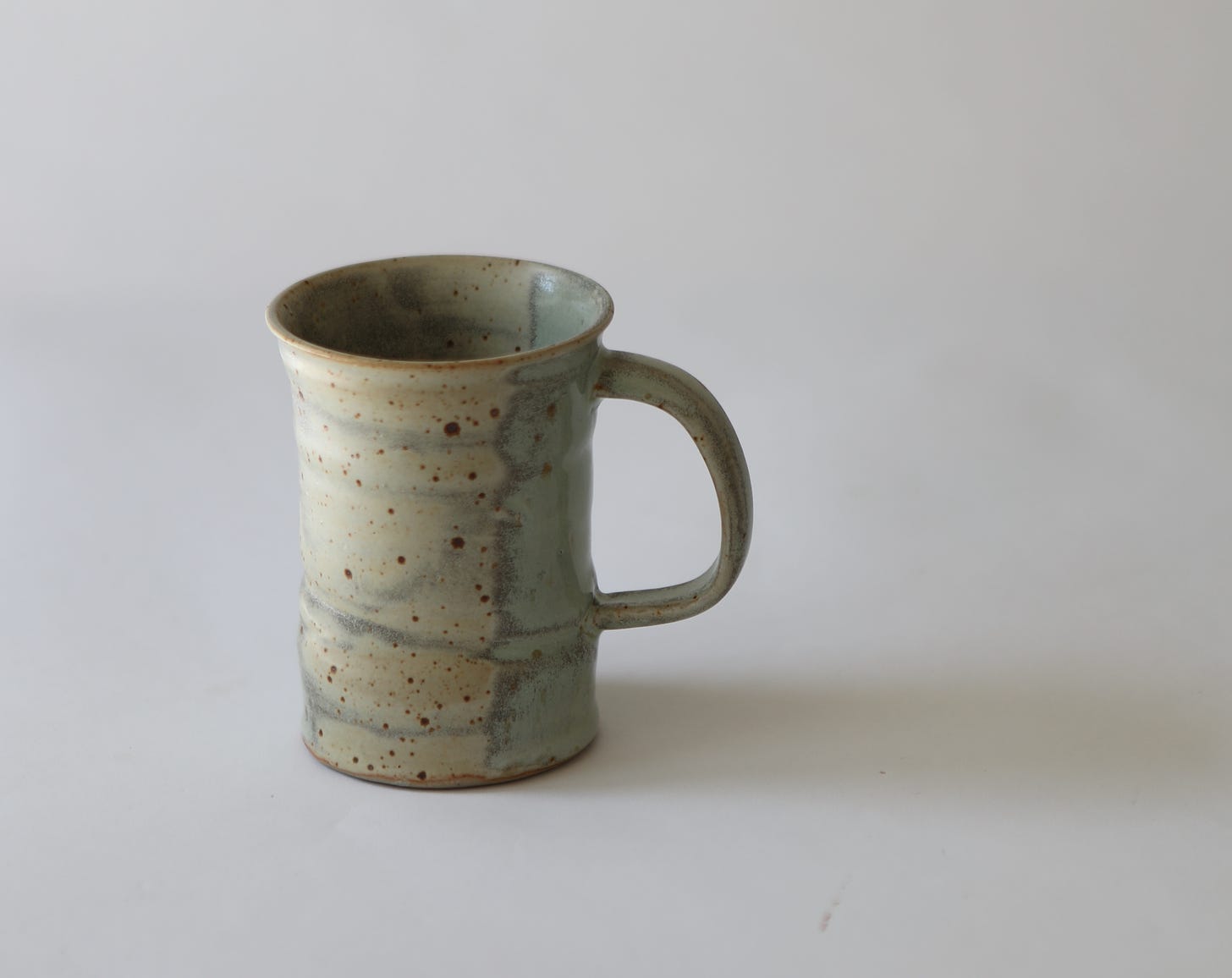 Yellow glazed mug with gray background, speckled with brown spots and some blue on one side. mug was thrown and altered. The brown spots are like the surface of a bird's egg.