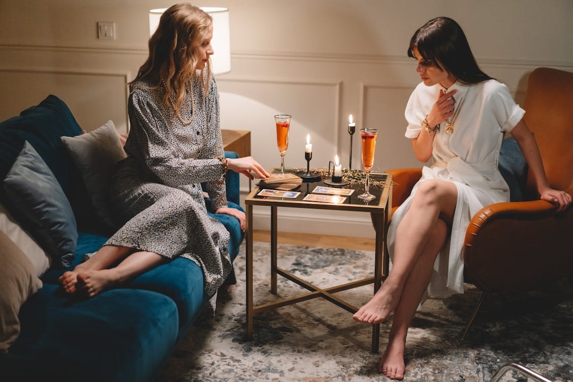 Free Two women enjoying a tarot reading session with candles and wine in a cozy indoor setting. Stock Photo