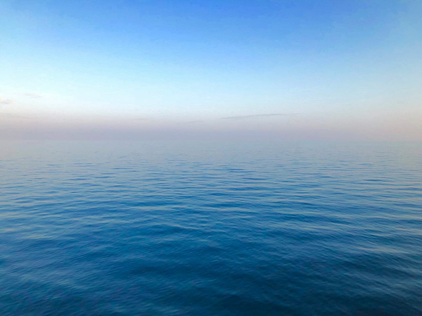  A misty, hazy horizon line out on the Mediterranean Sea. The muted steel-blue of the water turns into soft grey-pinks at the horizon line. There may or may not be land out there at the edge.