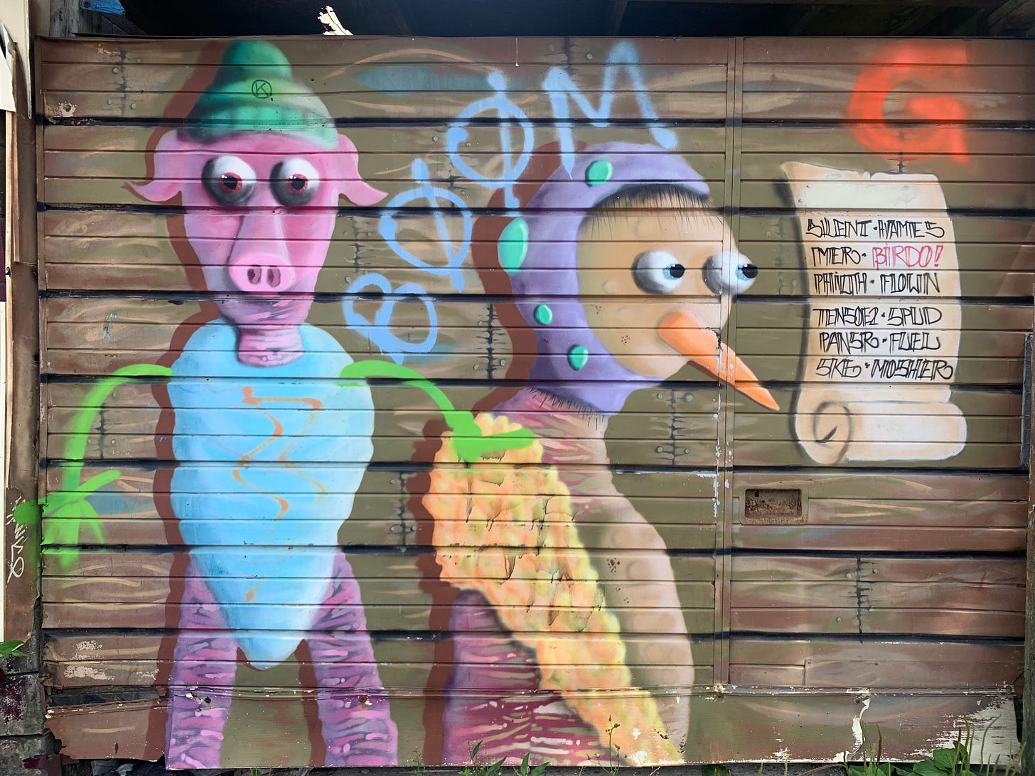 A spray-painted mural of a pig with a green toque and blue cotton-candy-like body and a bird wearing some sort of helmet, with a barely legible scroll to the right that says "BIRDO" in red among other black text. Both characters have very piercing eyes and no eyelids.