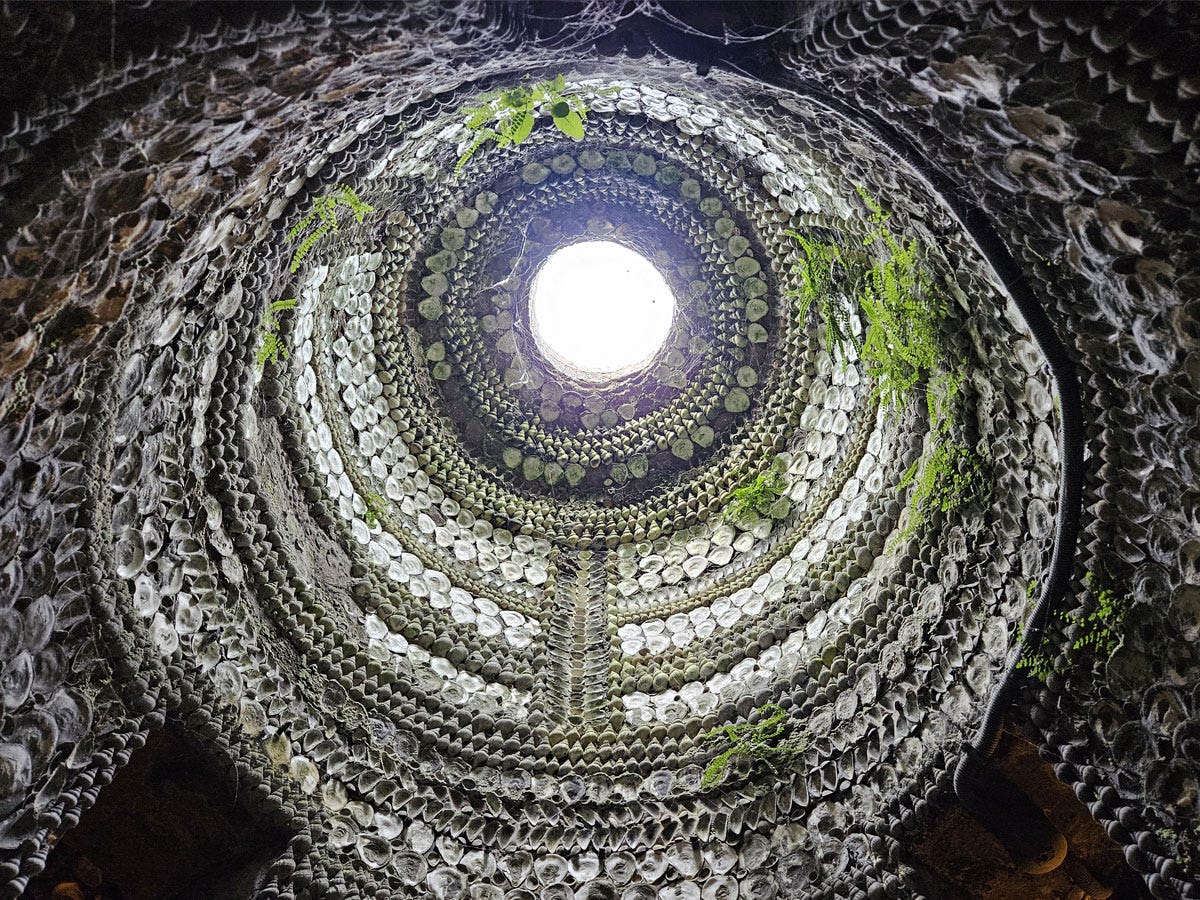 A view into a ceiing dome which features a skylight at its centre. The surface of the dome is covered in shells.