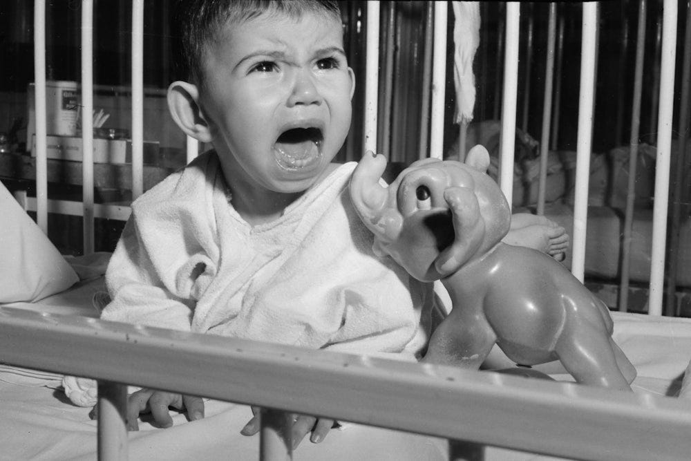 A very unhappy toddler screams in his crib.