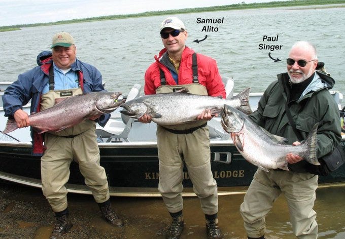 Photo of three men in fishing gear, standing next to a small boat while showing off king salmon they apparently caught. The man in the center is Supreme Court Justice Samuel Alito. To the right of Alito is hedge fund billionaire Paul Singer. The third man is not identified. 
