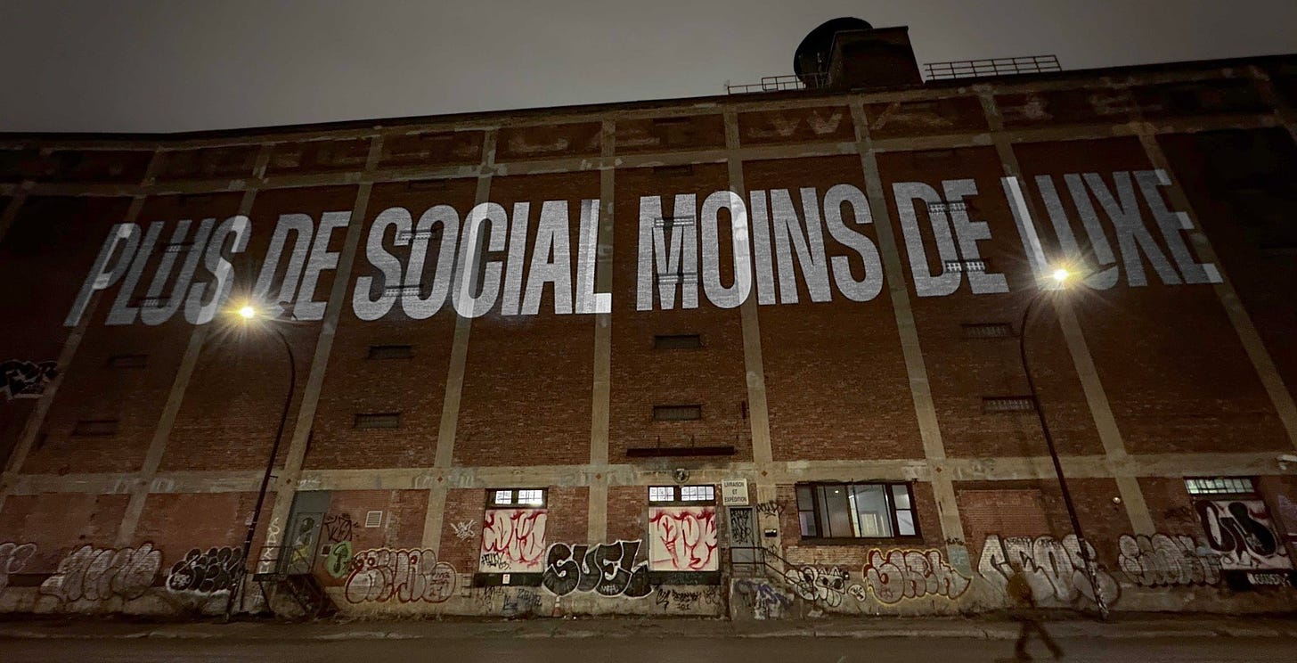 Projection sur l’entrepôt Van Horne, la nuit. On peut y lire: « PLUS DE SOCIAL MOINS DE LUXE »