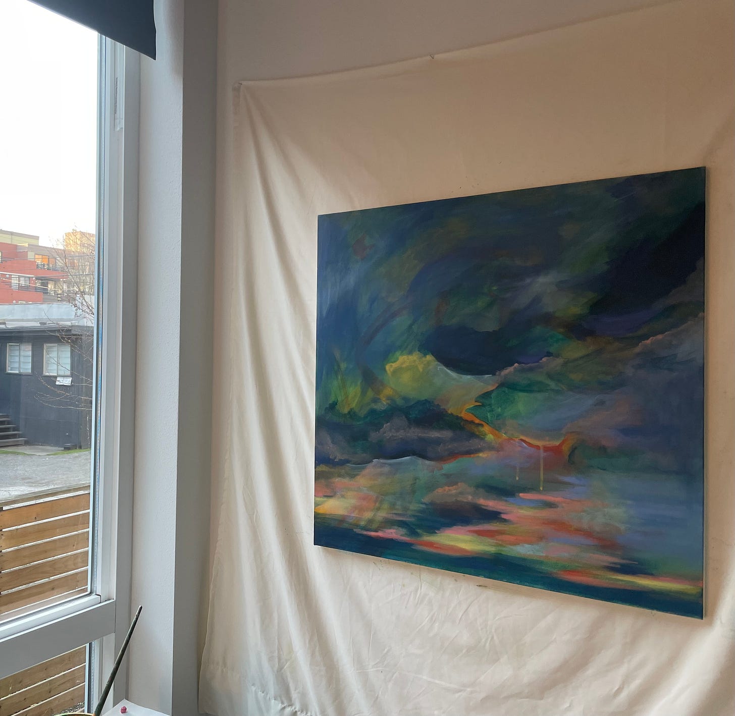 A painting of a sunset with dark blue clouds hanging on a wall next to a window