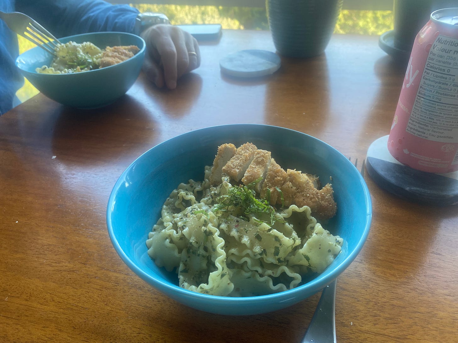 A blue bowl of the pasta described above, long noodles with lasagne-like ruffled edges. Basil chiffonade and slices of breaded nugget are on the top. 