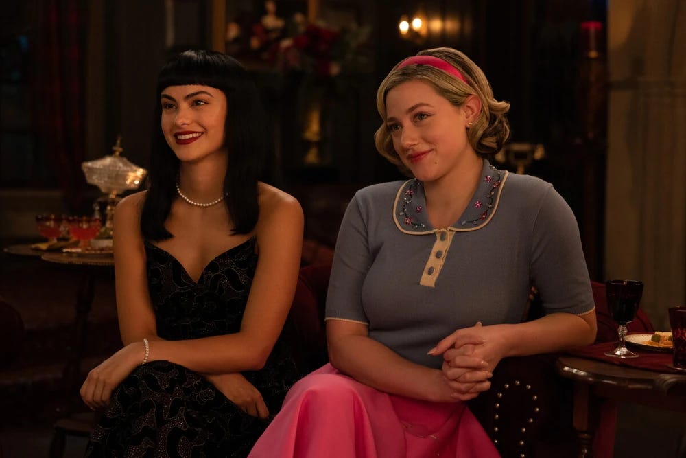 Veronica and Betty sitting down in their 50s attire.