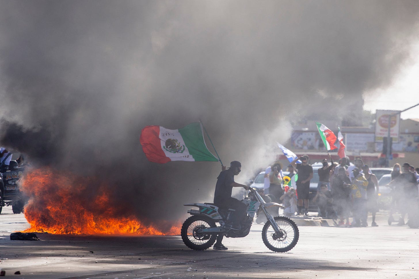 A demonstrator waving a Mexican national flag next to a car on fire in L.A.’s Compton neighborhood A demonstrator waving a Mexican national flag next to a car on fire in L.A.’s Compton neighborhood